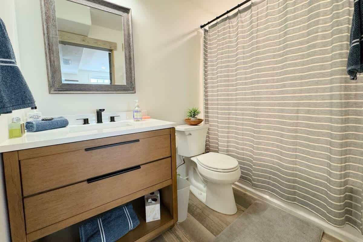 A bathroom with a wooden vanity, a white toilet, a striped shower curtain, and a mirror above the vanity.