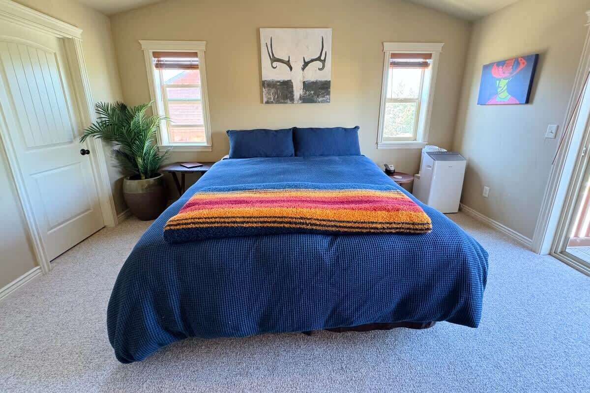 A bedroom with a bed, a large window, a potted plant, and a wall-mounted artwork.