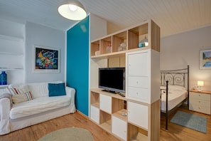 A room with a white sofa, a TV on a wooden stand, a bed, and a blue wall.
