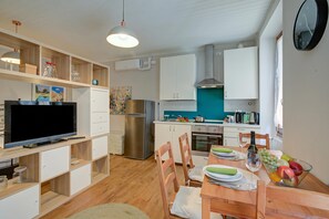 Eine kompakte Küche mit Fernseher, Kühlschrank, Backofen und Essecke mit Stühlen und Tisch.