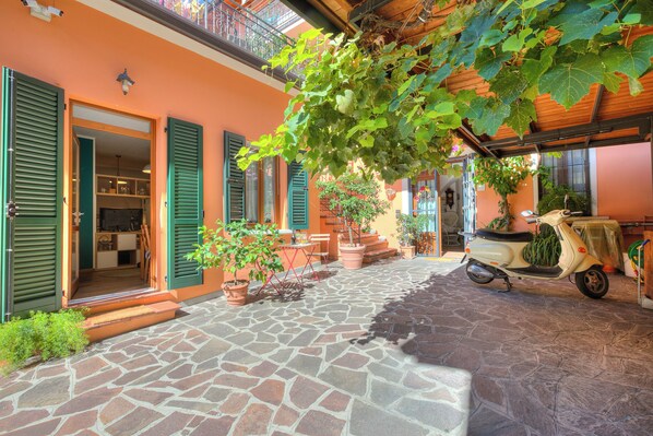 A courtyard with a stone floor, green shutters, a scooter, and potted plants. - Vicky Loft Gardone-relax & Vittoriale (Gardone Riviera)