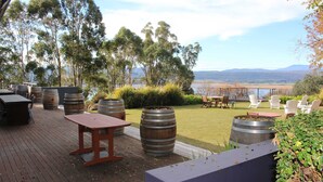 An outdoor patio with wooden flooring, metal barrels, and seating areas overlooking a natural landscape.