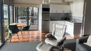 A modern kitchen with white cabinets, a dining area with a wooden table and green chairs, and a leather chair.