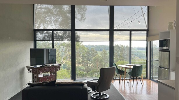 A modern room with a large window, a television, a dining table with chairs, and a kitchen area.