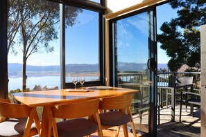 A wooden table with chairs, a glass partition, and a view of a lake and mountains. - The Tamar Ridge Lookout 2Bed 2Bath Suite (Grindelwald)