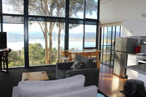 A modern living room with a large window, a sofa, a dining table, and a kitchen area. - The Tamar Ridge Lookout 2Bed 2Bath Suite (Grindelwald)