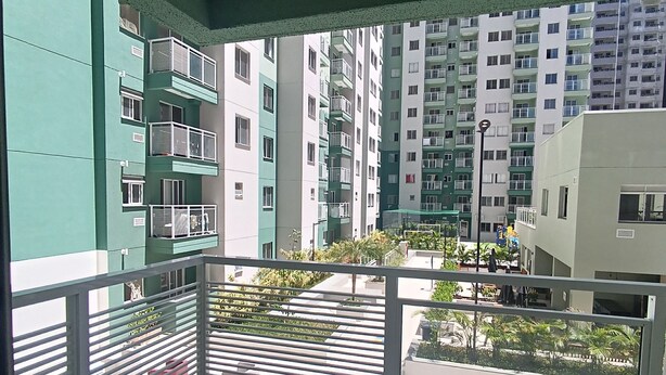 A balcony with a view of multi-story buildings, a street with parked cars, and outdoor seating.