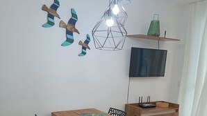 A dining area with a wooden table and black chairs, a TV mounted on the wall, and a shelf with decorative items.