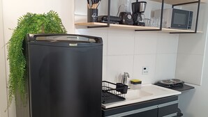 A modern kitchen with a black refrigerator, a microwave, and a coffee maker on a shelf.