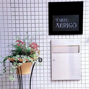 A tiled wall with a framed sign reading 'TABIU XBRIGO' and a potted plant with hanging vines. - Arima Onsen Abrigo (Kobe)