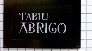 Un letrero negro con letras blancas que dice 'TABIU ABRIGO' sobre una pared de azulejos.