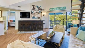 A modern living room with a bar area, a sofa, a coffee table, and a balcony with outdoor seating.