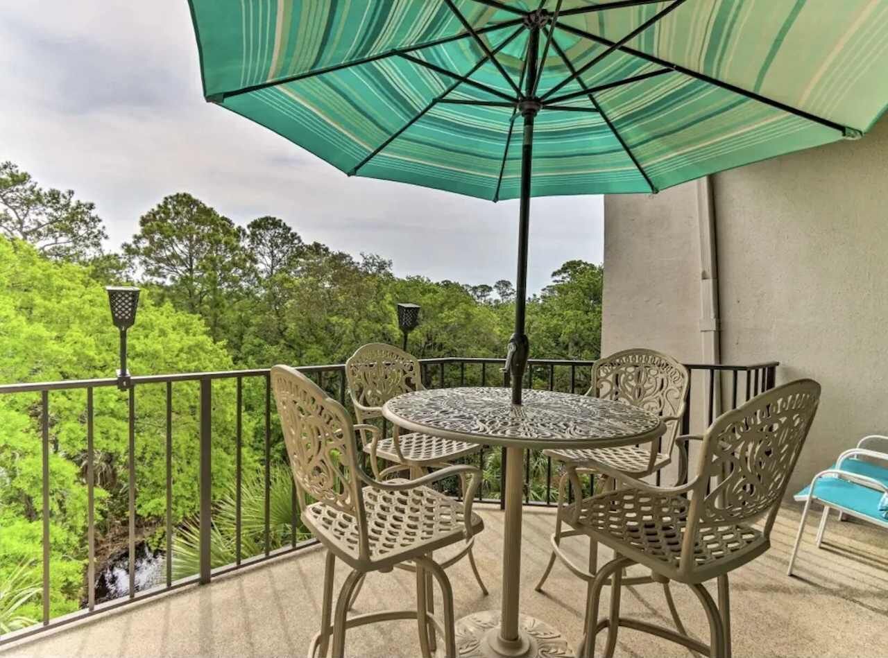 Un balcon avec une table ronde et quatre chaises, un parasol et une vue sur une végétation luxuriante.