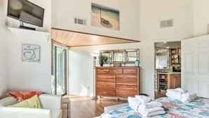 A bedroom with a bed, a dresser, a TV, and a bathroom visible through an open door.