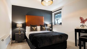 A bedroom with a large bed, two bedside tables, a nightstand, a desk, and a window with a view. - The Arran Suite - Your Stylish Scottish Getaway! (Glasgow)