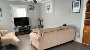Ett vardagsrum med en beige soffa, en tv som står på ett TV-bord och ett träskåp.