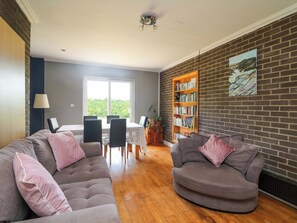 Ein Wohnzimmer mit einer Couch, Sesseln, einem Esstisch und einem Bücherregal.