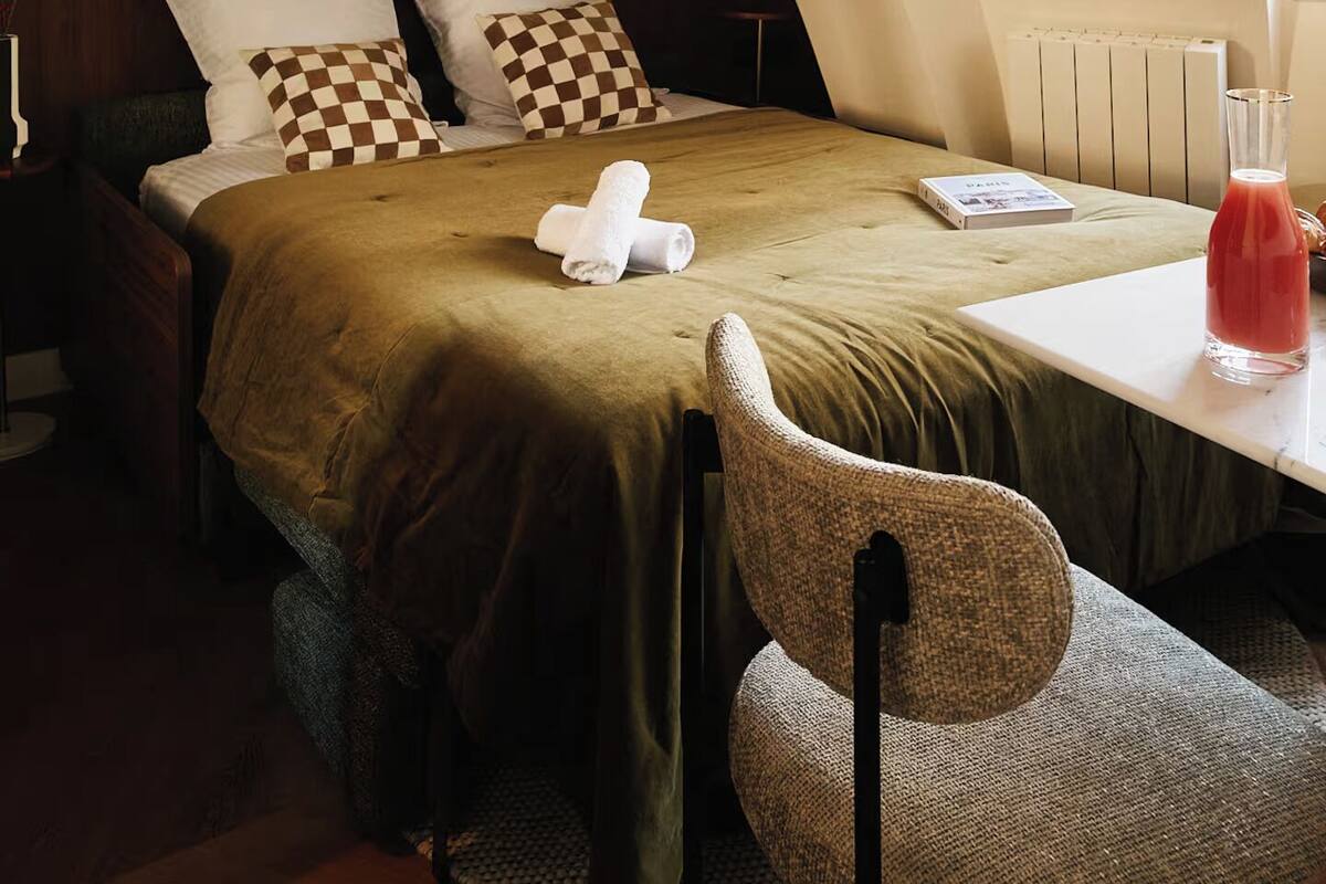 A bedroom with a bed, a chair, a table, a mirror, and a ceiling light fixture.