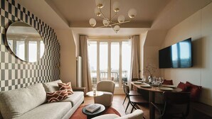 A modern living room with a checkered wall, a round mirror, a sofa, a coffee table, a dining area with chairs and a TV mounted on the wall. - Résidence Louvre  (Paris)