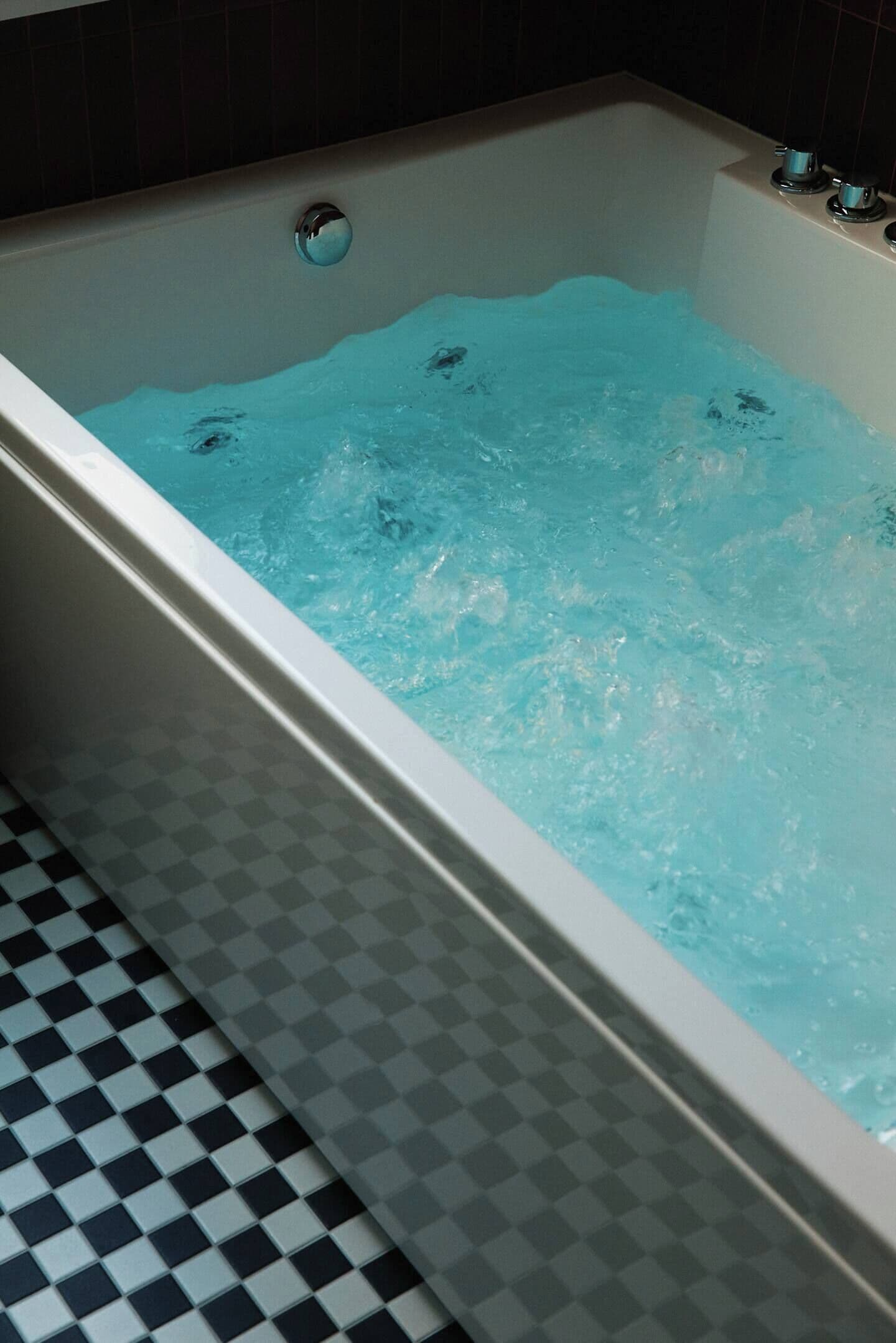 A bathtub with running water, a checkered floor, and a dark wall.