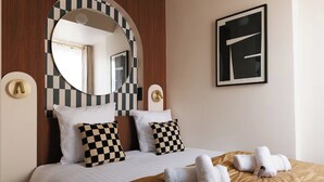 A hotel room with a large bed, checkered pillows, a round mirror, and a framed abstract artwork on the wall. - Résidence Louvre  (Paris)