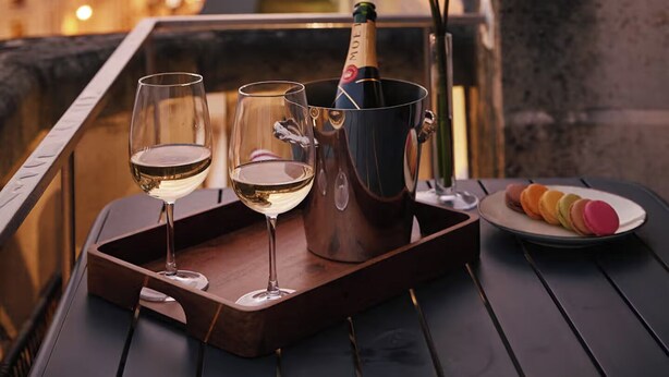 A balcony with a tray holding two wine glasses, a bottle of champagne, and a plate of macarons. - Résidence Louvre  (Paris)