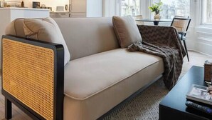 A modern living room with a sofa, a coffee table, and a patterned rug. There is a kitchen in the background with cabinets and a window.