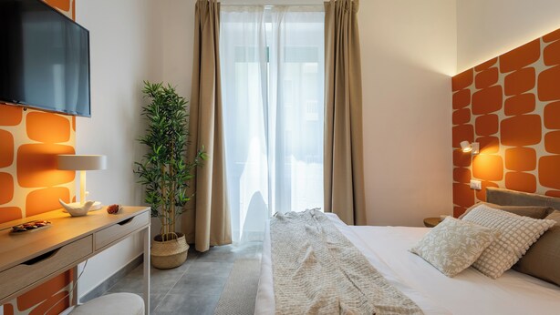 A modern hotel room with a bed, a TV, a desk, and a potted plant. - Cornelia Vatican Suites (Rome)