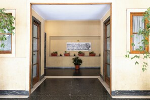 A hallway with a reception desk, potted plants, and a framed cityscape artwork on the wall. - Cornelia Vatican Suites (Rome)