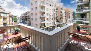 A balcony with a table and chairs, overlooking a street with multi-story buildings. - Cornelia Vatican Suites (Rome)