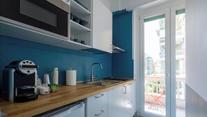 A modern kitchen with white cabinets, a wooden countertop, a coffee machine, and a view of a balcony with a red chair. - Cornelia Vatican Suites (Rome)