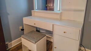 Un tocador blanc amb mirall i llums LED, una banca i una porta amb mànec de bronze.