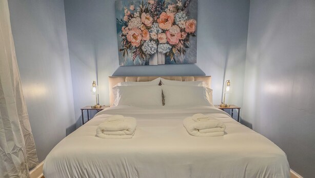 Un llit ben fet amb dues tovalloles doblegades, un quadre floral gran a la paret i dues làmpades de nit.
