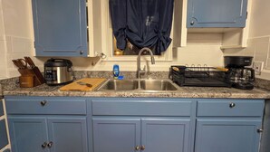 Cuina amb armaris blaus, un rentaplat de stainless steel, una cafetera i una taula de tallar.