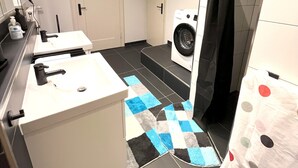 Een moderne badkamer met een wit wastafel, een zwart-wit geruit tapijt, een wasmachine en een douchegordijn met stippen.