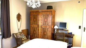 Een slaapkamer met een groot bed, een kledingkast, een bureau met een computer, een stoel en een kroonluchter.