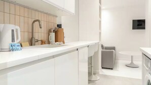 A modern kitchen with a white countertop, a kettle, a coffee maker, and a sink. - Résidence Greffulhe (Paris)