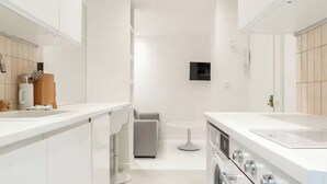 A modern kitchen with white cabinetry, a built-in oven, and a large sink. - Résidence Greffulhe (Paris)