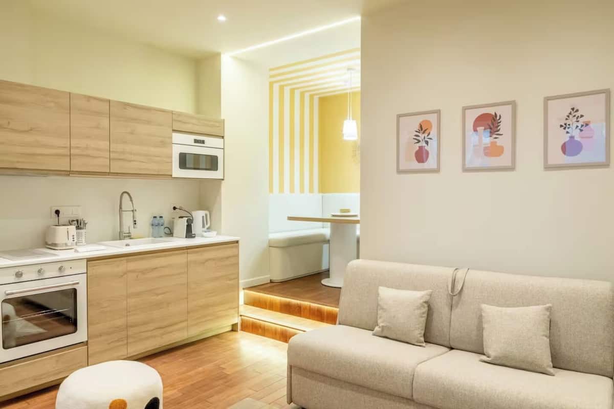 Une cuisine moderne avec des meubles en bois, un four encastré et un coin repas comprenant une table et des chaises blanches.