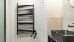 A modern bathroom with a black towel rack, a sink, and tiled walls. - Résidence Greffulhe (Paris)