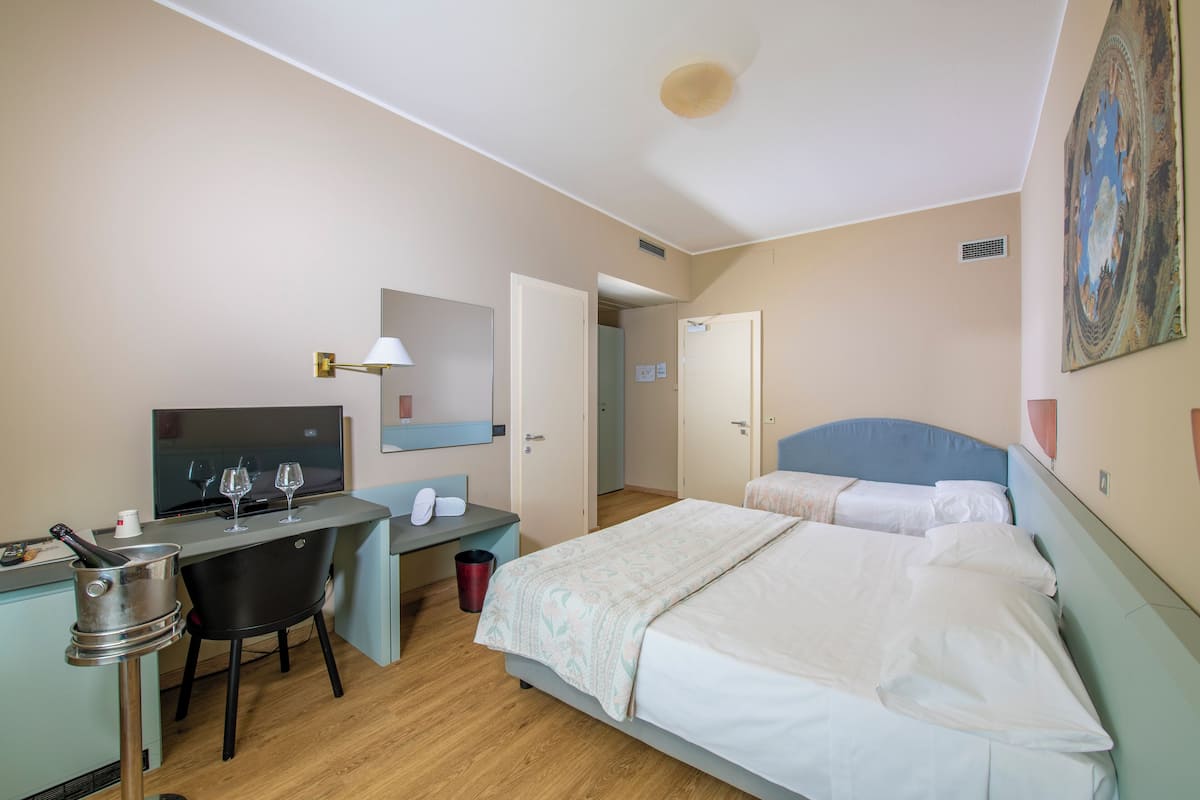 A hotel room with a bed, a desk with a computer and a chair, a TV, and a small kitchenette.