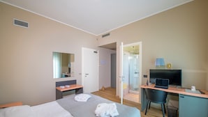A hotel room with a bed, a desk, a chair, a television, and a shower area.