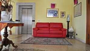 A living room with a red sofa, a patterned rug, a vase, and framed pictures on the wall.