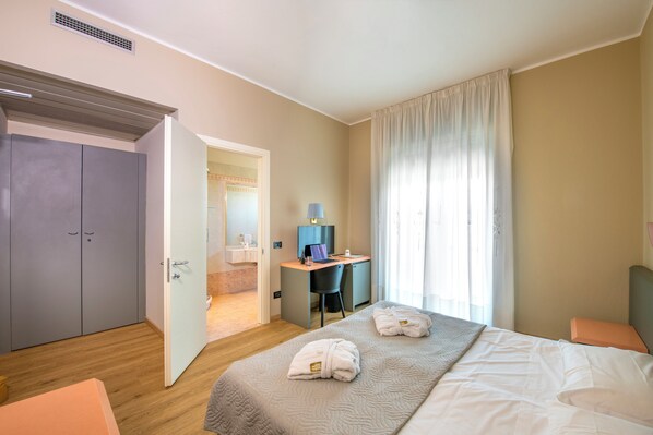 A hotel room with a bed, a desk, a chair, and a wardrobe.