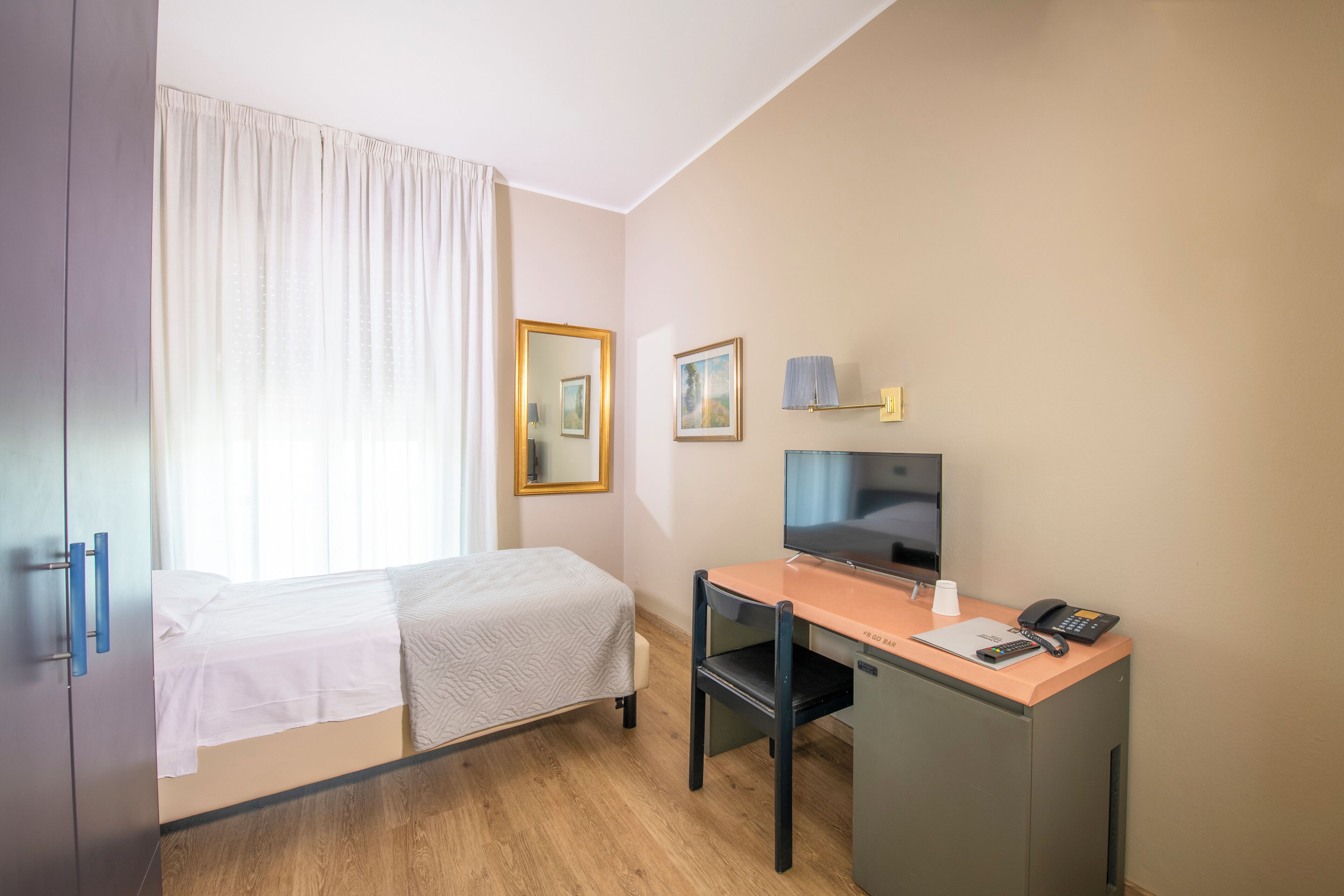 A hotel room with a bed, a desk with a computer, a telephone, and a television.