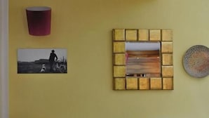 A room with two white armchairs, a yellow wall, a framed picture, and a decorative mirror.