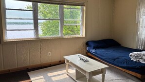 Une chambre avec un lit, une fenêtre donnant sur un plan d’eau, une petite table et un sol recouvert d’une moquette.