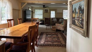 Un salon spacieux avec une table à manger en bois, des sièges confortables, un tapis à motifs et un tableau encadré accroché au mur.