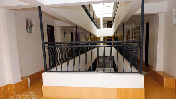 Un interior moderno con una escalera central, paredes blancas y suelo de madera.