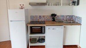 Eine kompakte Küche mit einem weißen Kühlschrank, einem Einbauofen, einer Spülmaschine und einer Mikrowelle.
